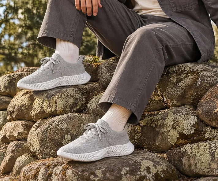 Person resting on a stone wall in gray Braidge sneakers