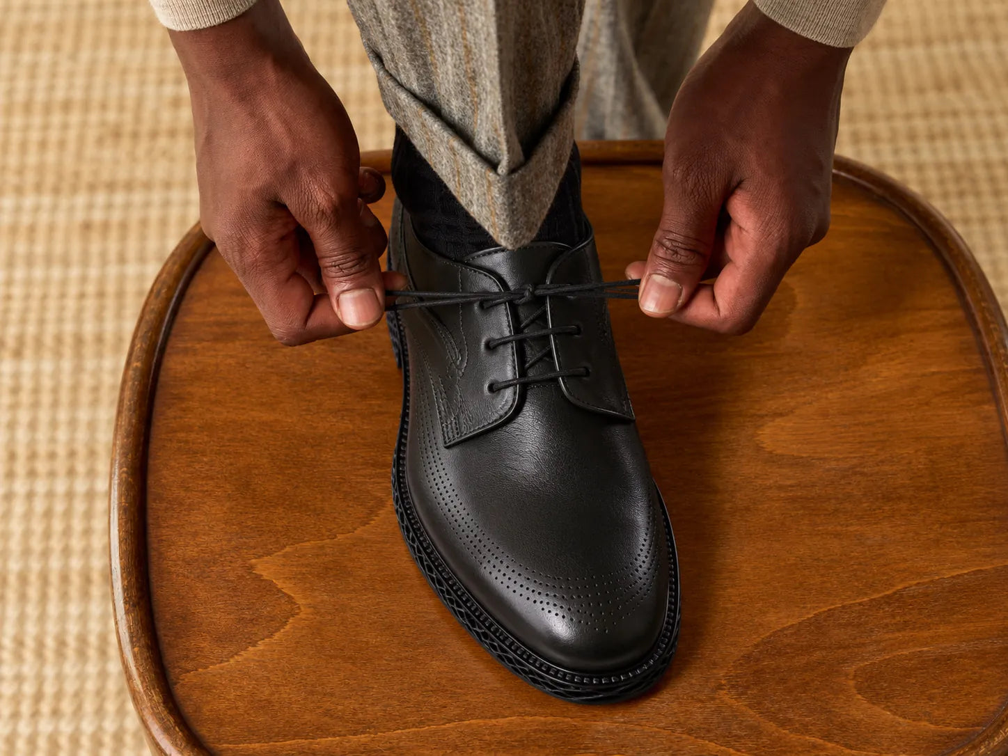 Hands lacing a black full-grain leather Derby shoe with brogue detail
